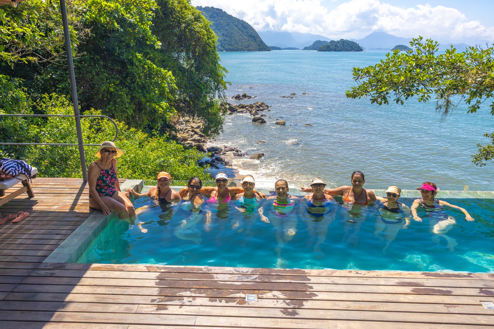 Alunas da Minha Melhor Vida juntas na piscina com o mar de Paraty ao fundo